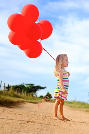 Young caucasian girl walks along a path, holding a bunch of helium filled red balloons @Warren Goldswain